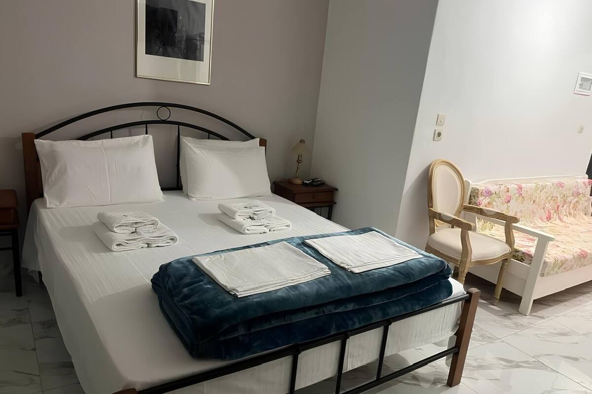 Un lit bien fait, avec du linge de lit et des serviettes blanches, une tête de lit rembourrée bleue et une table de chevet en bois avec une lampe.