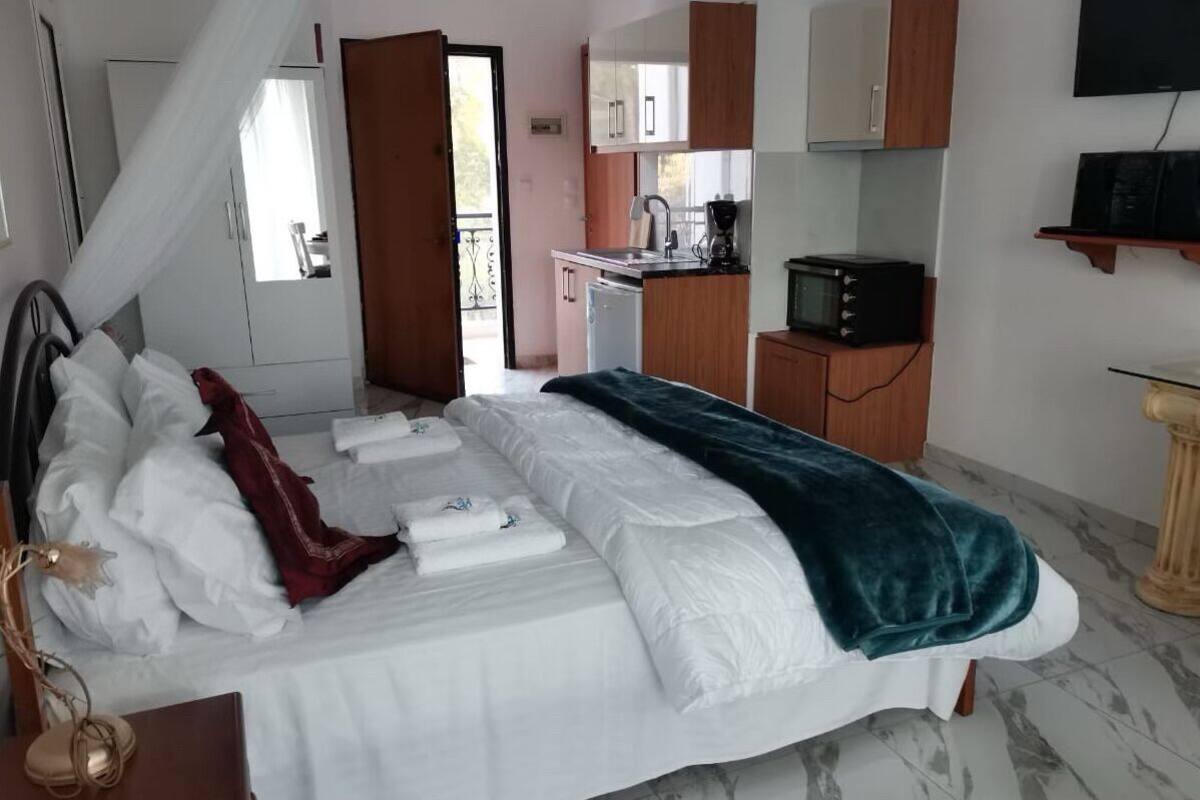 Une chambre avec un lit, une table de chevet, une télévision, un petit coin cuisine et un balcon.