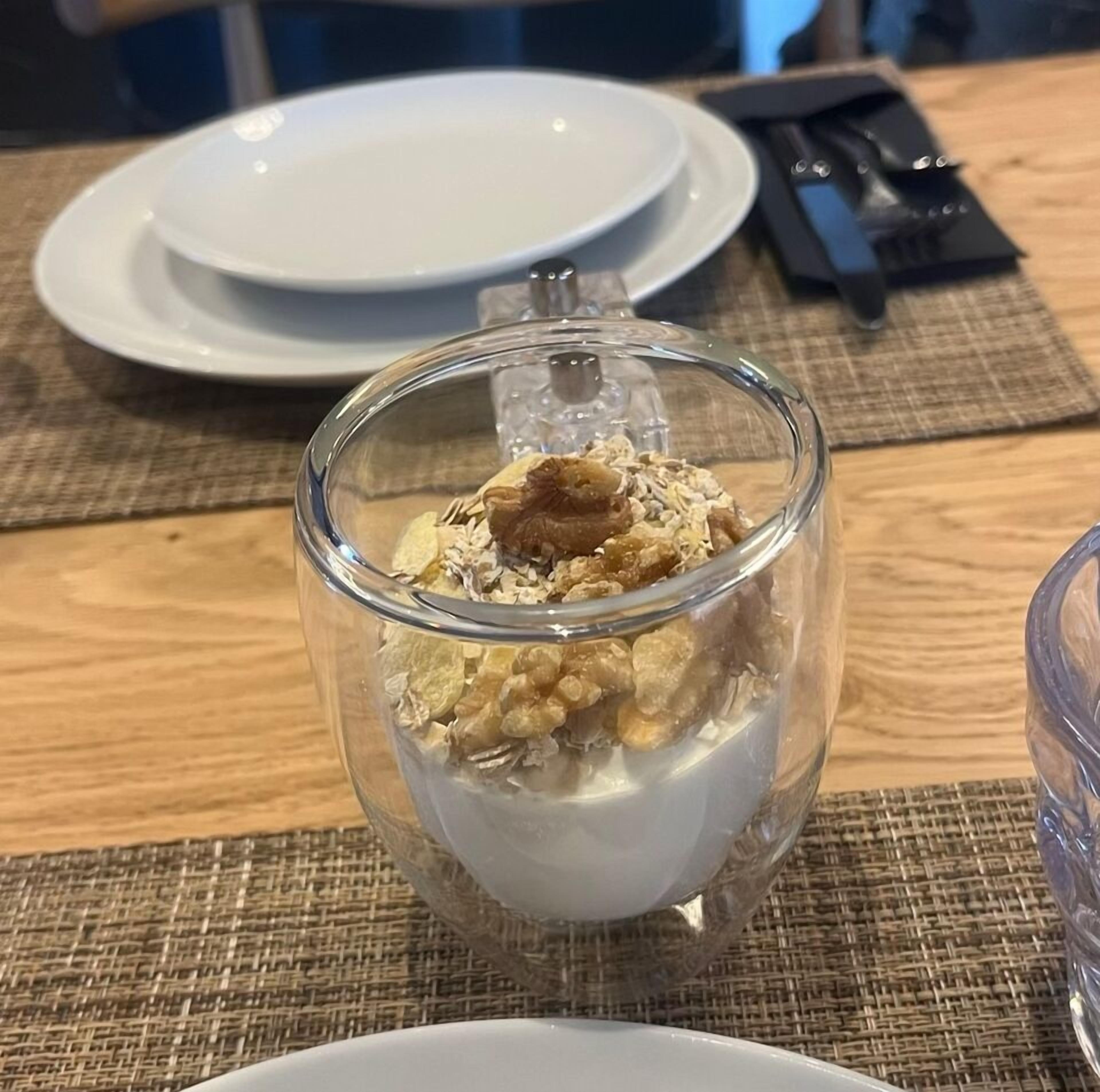 Una ciotola di vetro trasparente con un dessert a base cremosa e una copertura di biscotti sbriciolati o torta.