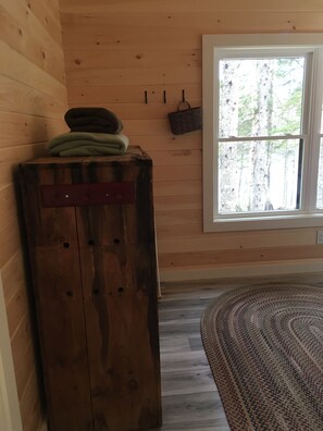 A wooden cabin interior with a large window, a wooden cabinet, and a patterned rug. - Secluded Lakefront, Dog-Friendly Cabin with Canoe, 7 Miles from the Ocean (Marshfield)