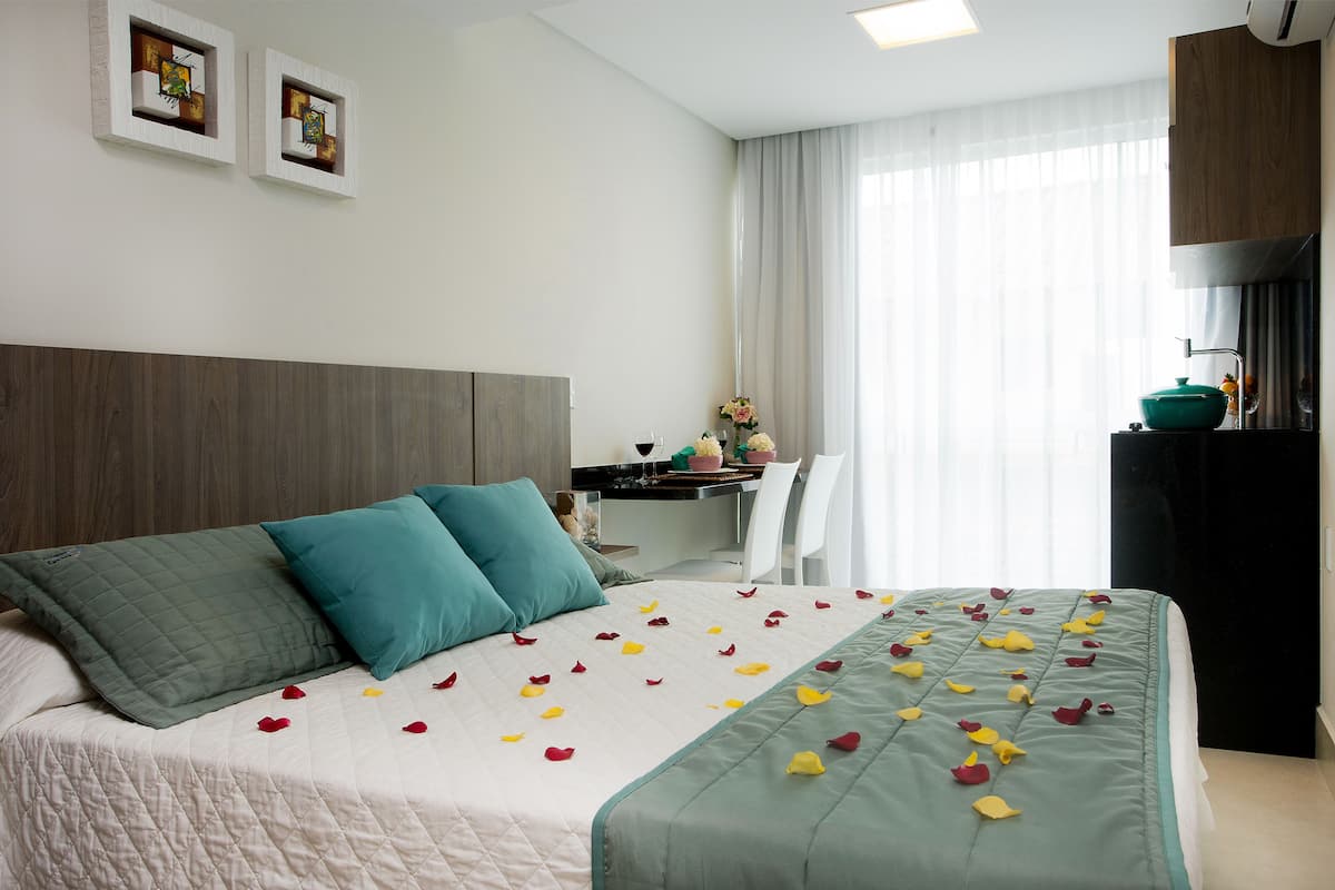 Una cama bien tendida con un cubrecolcha acolchado, dos almohadas turquesa y pétalos de rosa esparcidos.