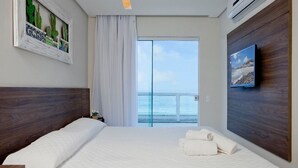 Hotelkamer met een groot bed, uitzicht op zee door een schuifdeur, een schilderij van cactussen en een wandtelevisie.