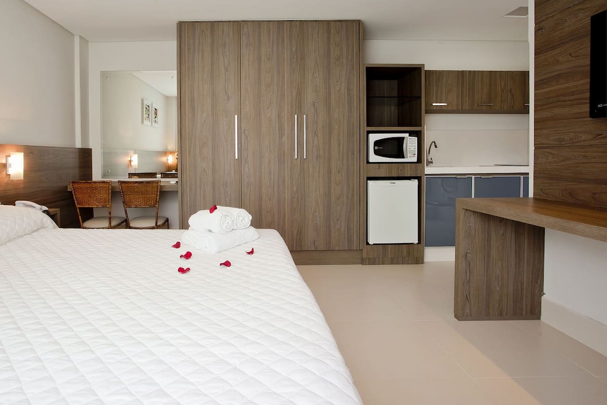 Una habitación de hotel con una cama grande, un armario, una kitchenette y un área de descanso con sillas.
