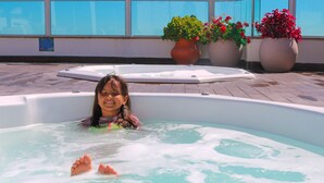 Iemand in een jacuzzi met een betegeld terras en plantenpotten op de achtergrond.