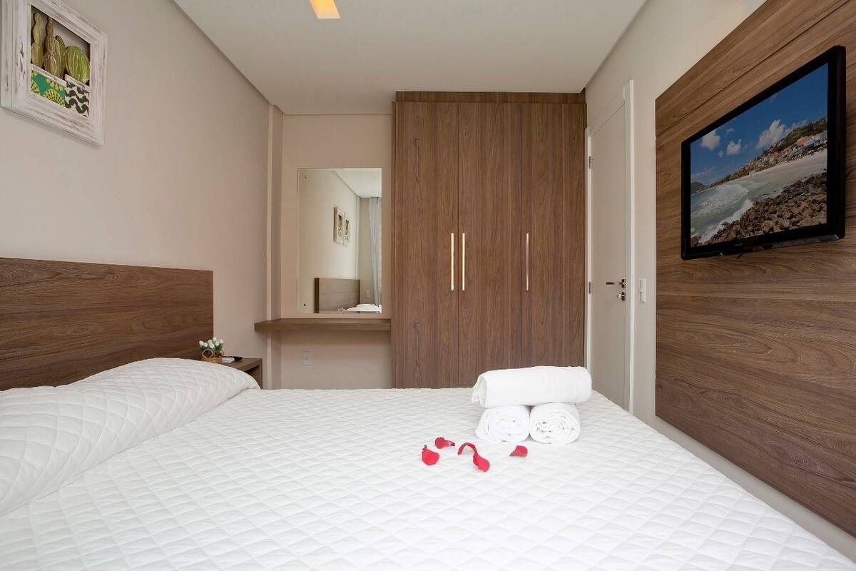 Habitación de hotel con una cama grande, un armario de madera, un televisor montado en la pared y un cuadro enmarcado sobre la cama.