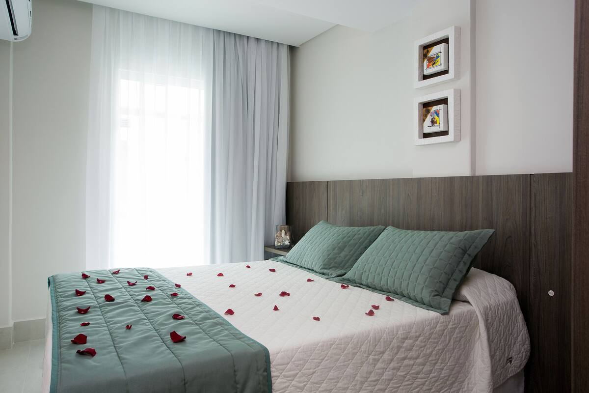 Una cama impecablemente hecha adornada con pétalos de rosa, un cabecero de madera y dos cuadros en la pared.