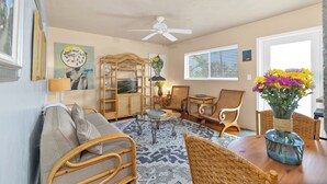 A cozy living room with a television, wicker furniture, a ceiling fan, and a vase of flowers. - Relaxed Beach living - 1 Bed/1 Bath with Private Garden, steps to Ocean (Hollywood)