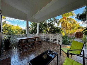 A covered outdoor area with a wooden bench, a table, and a chair.