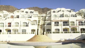 Een resort met een zwembad, meerdere balkons en een bergachtige achtergrond.