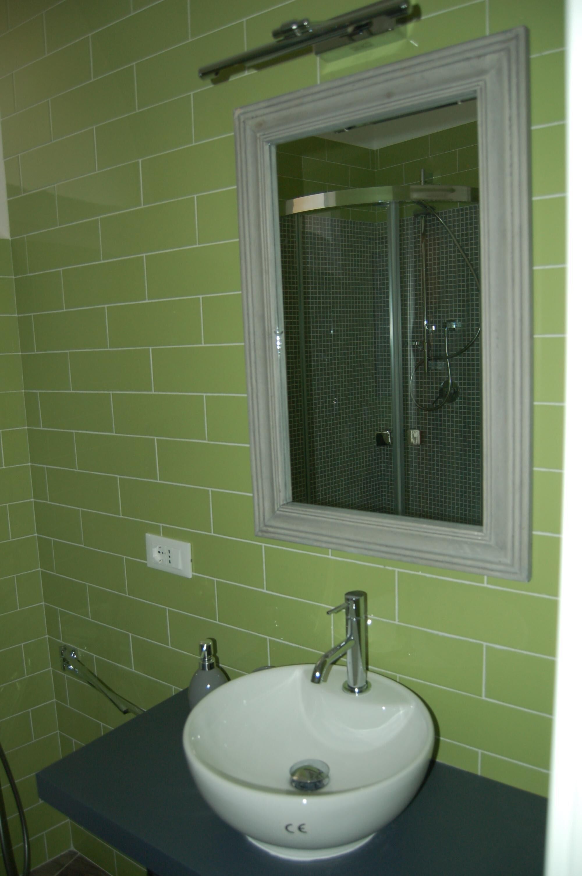 A bathroom with green tiles, a white sink, and a mirror above it.