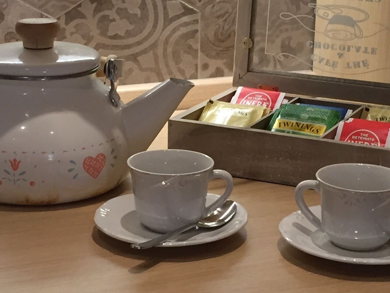 A table with two white cups and saucers, a teapot, and a box of tea bags.