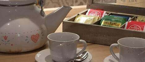 A table with two white cups and saucers, a teapot, and a box of tea bags.
