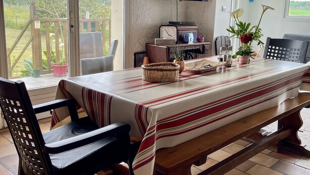 A dining area with a long table, chairs, a TV mounted on the wall, and a view of the outdoors. - for rent Aignan Gers (French Tuscan) (Aignan)