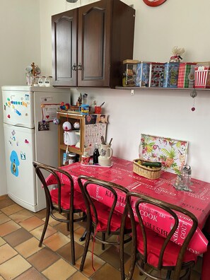 A kitchen with a red tablecloth, wooden chairs, a refrigerator with magnets, and a cabinet above. - for rent Aignan Gers (French Tuscan) (Aignan)