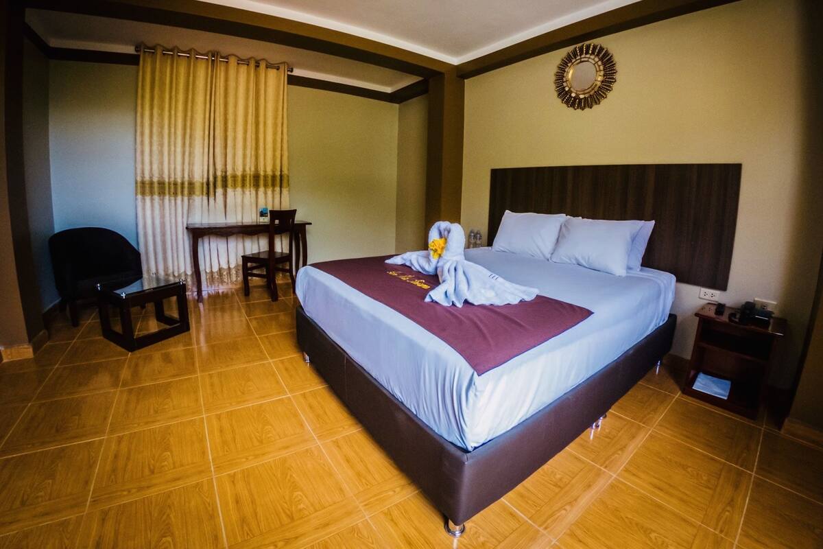A hotel room with a large bed, a desk, a chair, and a small table.