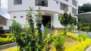 Un edificio moderno con un área exterior cubierta, piscina y jardines bien cuidados.