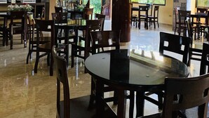 Un restaurante con techo alto, vigas de madera y una gran pantalla de televisión. Mesas y sillas dispuestas para comer.