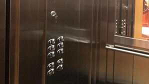 Interior de un ascensor con paredes metálicas, un panel de control con botones y un techo con diseño de cuadrícula.
