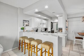 A modern kitchen with white cabinets, a marble countertop, and a central island with bar stools. - Private Beachfront on Siesta Key (Siesta Key)