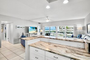 A modern kitchen with a large island, a view of the beach, and a ceiling fan.