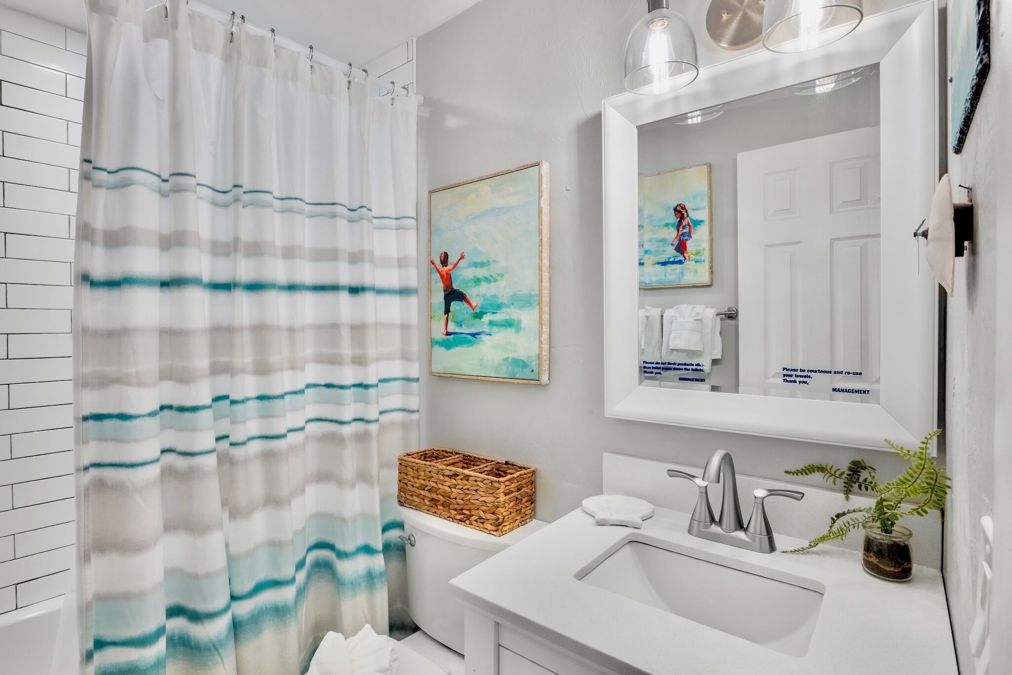 A modern bathroom with a shower curtain, a sink, a mirror, and two framed artworks.