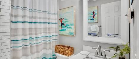 A modern bathroom with a shower curtain, a sink, a mirror, and two framed artworks.