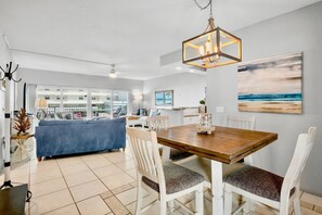 A spacious dining area with a wooden table and white chairs, a chandelier, and a view of the balcony. - Private Beachfront on Siesta Key (Siesta Key)