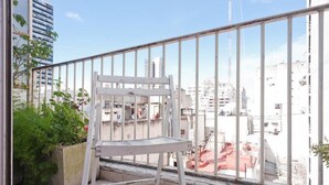 A balcony with a white chair, a concrete planter with green plants, and a cityscape view. - Historico Duplex en el Centro (Buenos Aires)