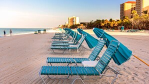 Una hilera de sillas de playa en una arena con vistas despejadas al océano y edificios al fondo.