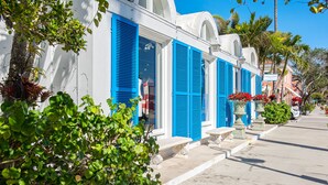 Una hilera de edificios blancos con contraventanas azules, cielo despejado y vegetación.