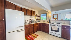 A compact kitchen with wooden cabinets, a white refrigerator, a microwave, a stove, and a window with a view.
