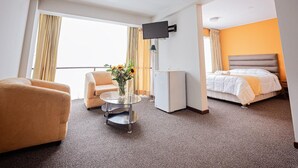 A hotel room with a bed, a sofa, a small table with a vase of flowers, a TV mounted on the wall, and a window with curtains. - Hotel San Felipe Suites (Arequipa)