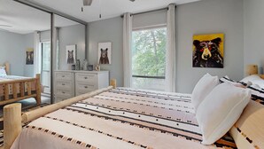 A bedroom with a bed, a wooden headboard, a ceiling fan, a window with curtains, and a painting on the wall.