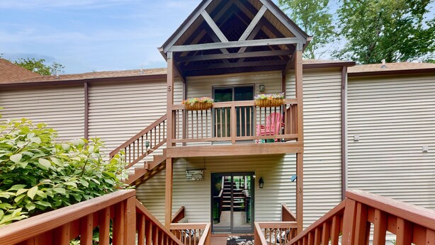 A two-story building with a wooden balcony, a staircase leading to the entrance, and a door with a welcome mat.