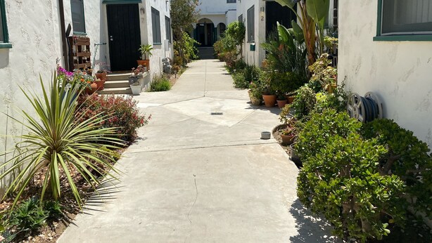 A narrow pathway flanked by white buildings with green trim, leading to a central entrance. - Bungulow on the beach (Long beacj)