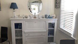 A white vanity with a mirror, a blue lamp, and decorative items on top. - Bungulow on the beach (Long beacj)