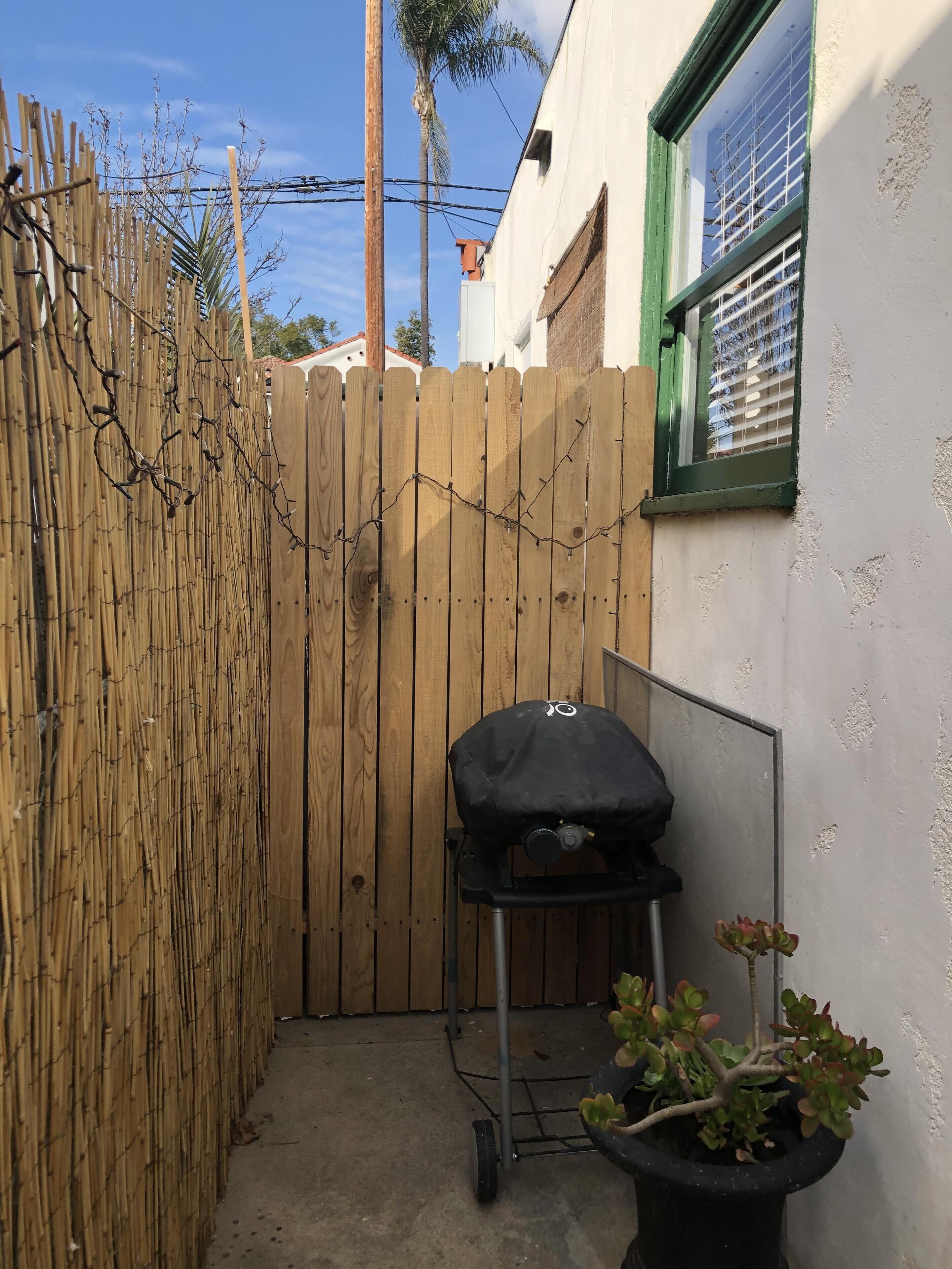 Un espacio exterior reducido con cerca de madera, una parrilla y una planta en maceta.
