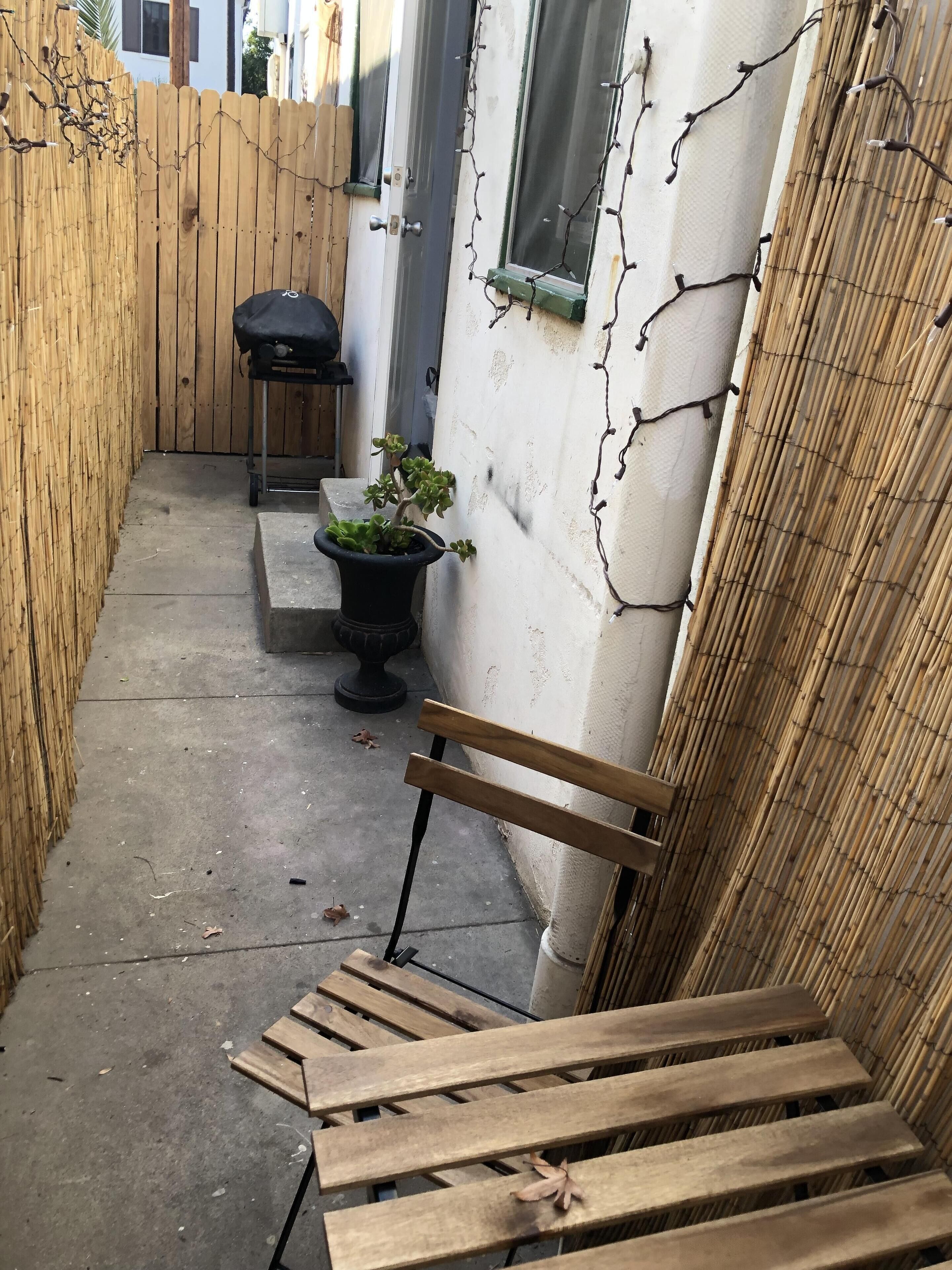 Eine schmale Außenveranda mit einer Holzbank, einem Blumentopf und einem kleinen Tisch.
