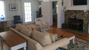 Un salon confortable avec un canapé, une petite table, un fauteuil en osier, une cheminée et un téléviseur.
