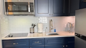 Une cuisine moderne avec des meubles de couleur bleu foncé, un four à micro-ondes en acier inoxydable et un four encastré.