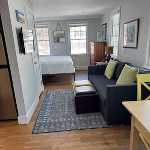 A compact living space with a bed, a sofa, a small table, and a cabinet. - West End Studio in a Waterfront Building (Provincetown)