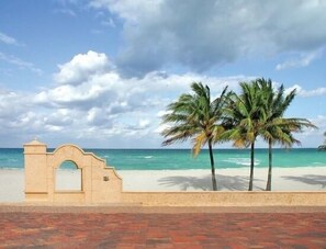 A beach with a clear sky, palm trees, and a stone archway.