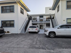 A modern two-story building with a central staircase, a covered driveway, and two parked cars.