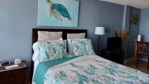 Une chambre à coucher avec un lit, une table de chevet, une lampe, une chaise et un tableau représentant une tortue accroché au mur.