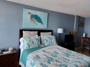 A bedroom with a bed, a nightstand, a lamp, a chair, and a painting of a turtle on the wall.