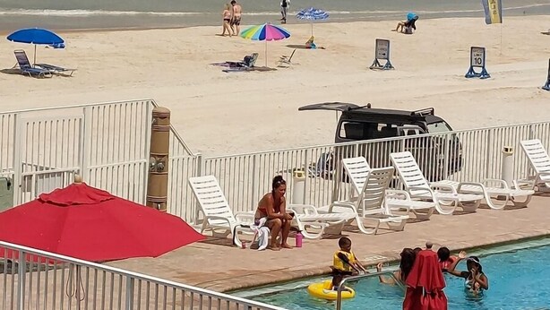 Une vue sur la plage avec une piscine, des chaises longues et des parasols.