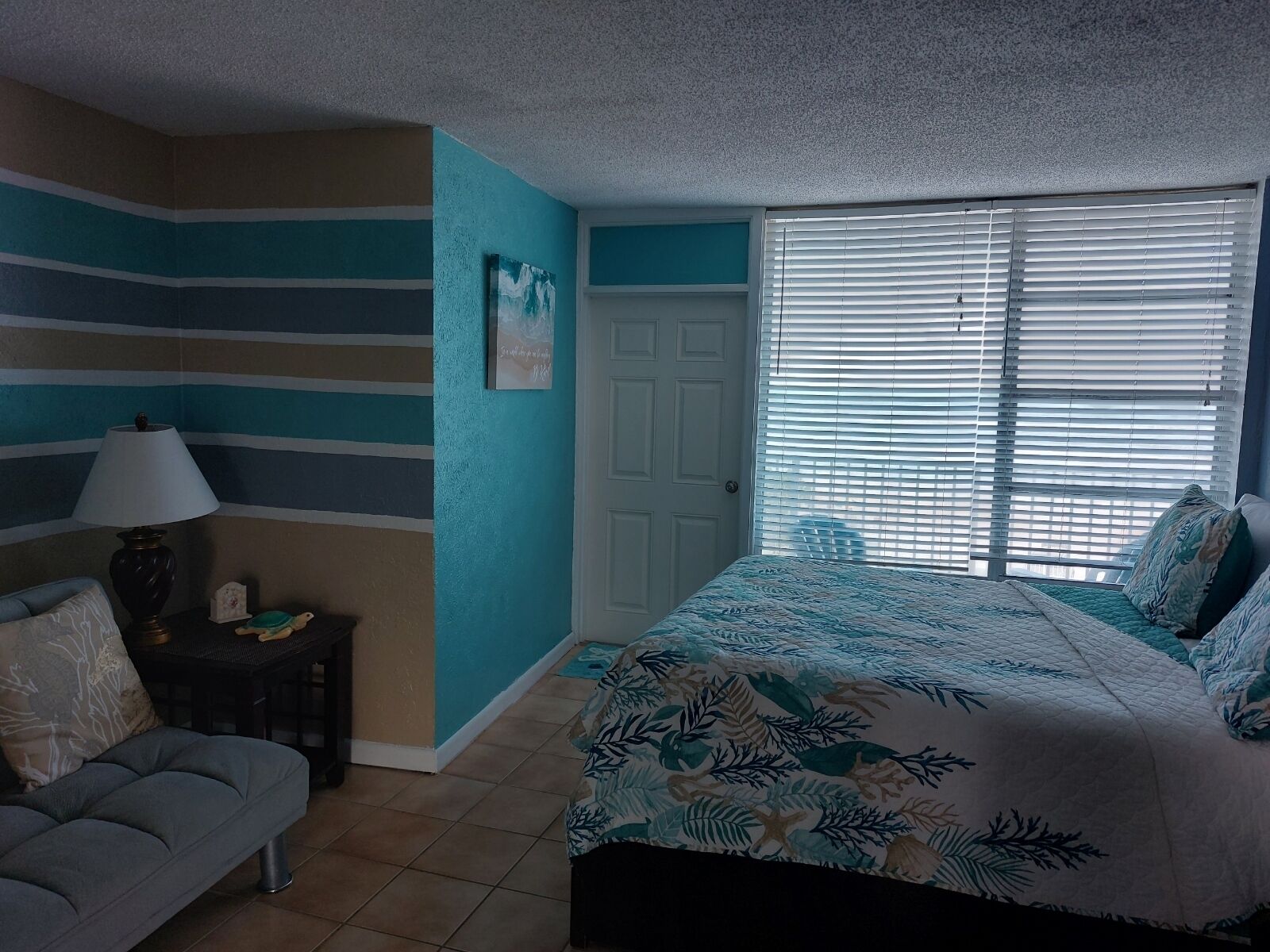 A bedroom with a bed, a chair, a nightstand, and a window with blinds.