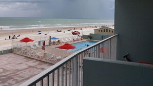 Un balcon avec vue sur une plage, une piscine et un ciel nuageux.