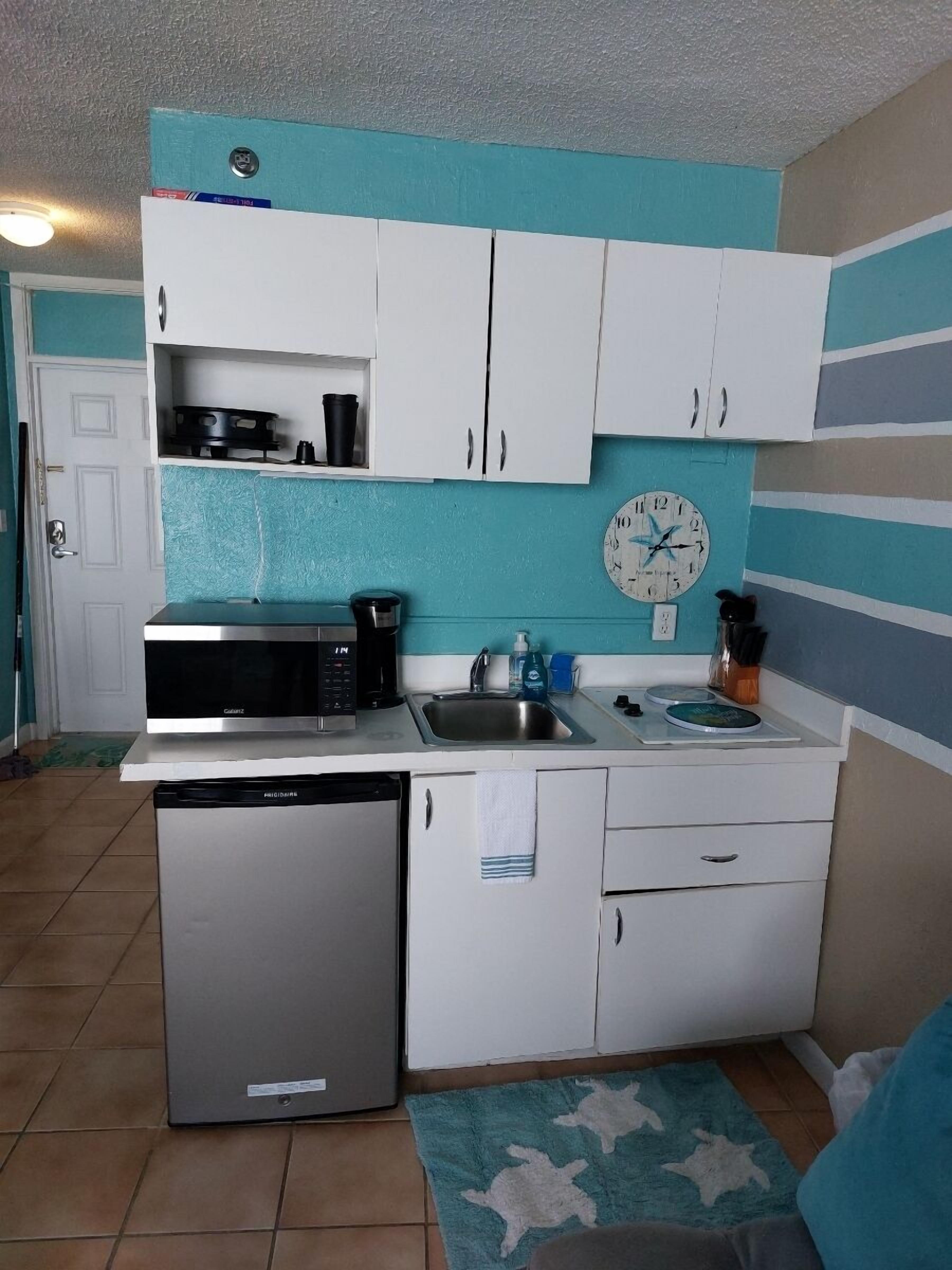 A compact kitchen with white cabinets, a microwave, a coffee maker, and a sink.