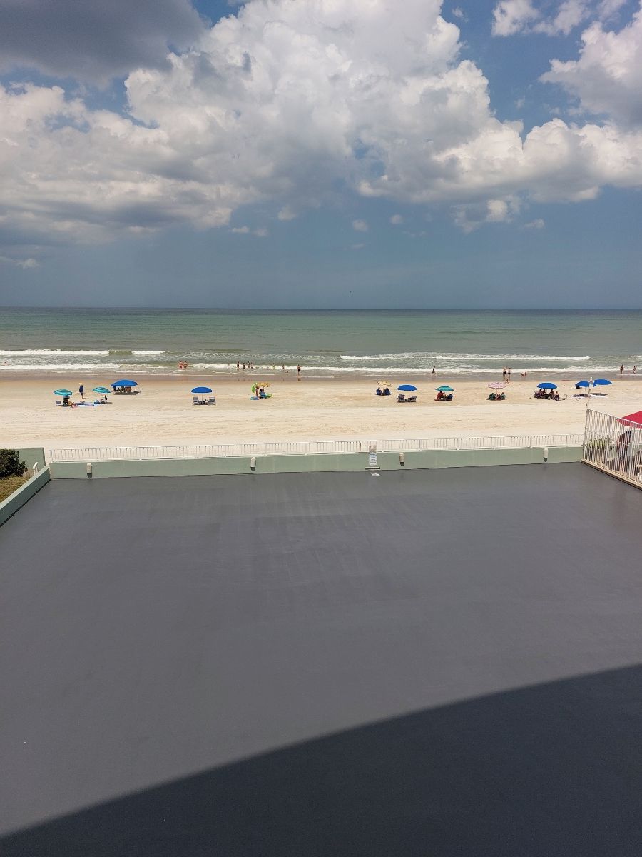 Une vue sur la plage depuis un balcon, avec un ciel dégagé, une plage de sable et plusieurs parasols.